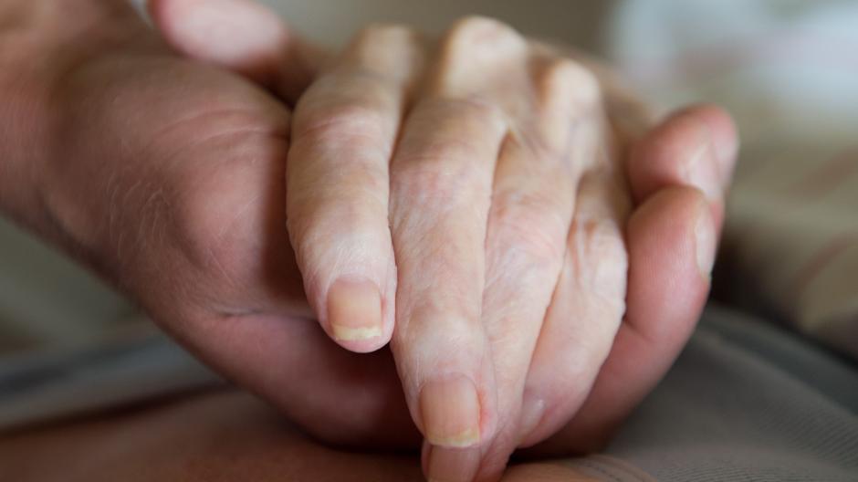 Ein Pfleger hält die Hand einer schwer kranken Frau: Ein Augsburger Arzt hilft Menschen, die nicht mehr weiterleben wollen, beim Suizid.