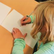 Ein Kind zeichnet ein auf einem Zettel abgebildetes Kreuz ab. Solche und ähnliche Aufgaben werden bei Schuleingangsuntersuchungen gestellt. 