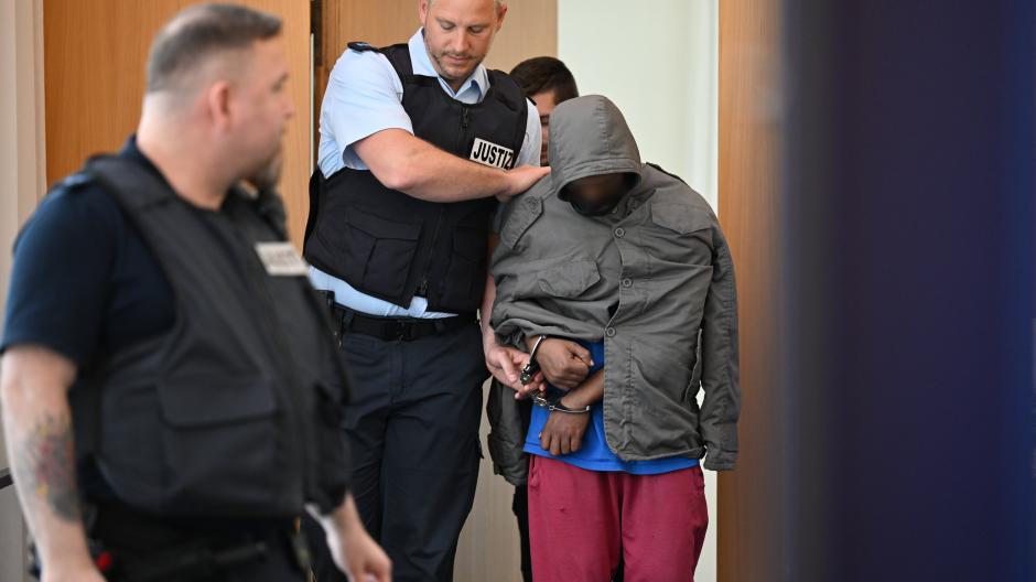 Der Angeklagte im Fall der tödlichen Messerattacke wird in Hand- und Fußschellen in den Gerichtssaal geführt. Der Asylbewerber aus Eritrea soll in Illerkirchberg zwei Schülerinnen mit einem Messer attackiert haben. Die 14-jährige Ece starb an ihren Verletzungen.