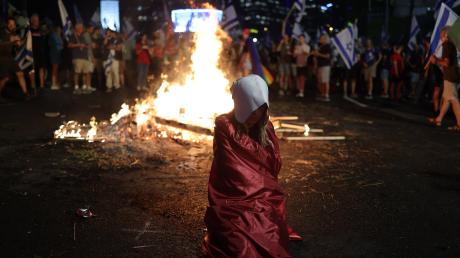 Eine Frau, gekleidet wie eine Figur aus der Fernsehserie "Handmaid's Tale", sitzt vor einem Feuer, während Demonstranten die Autobahn blockieren, um gegen die Pläne der Regierung von Premierminister Netanjahu zu protestieren.