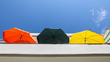 Drei Sonnenschirme stehen auf einem Balkon an einem Mehrfamilienhaus. Für den heutigen Tag sind Temperaturen über 30 Grad Celsius vorhergesagt.