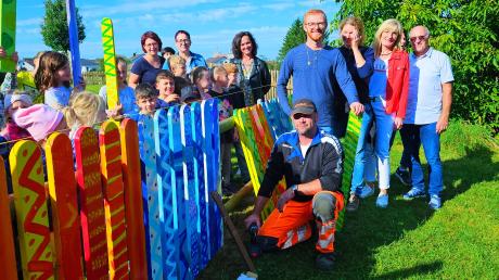 Die kleinen und großen Künstler und Künstlerinnen bringen ihren farbenfrohen Zaun am Gemeindespielplatz an.