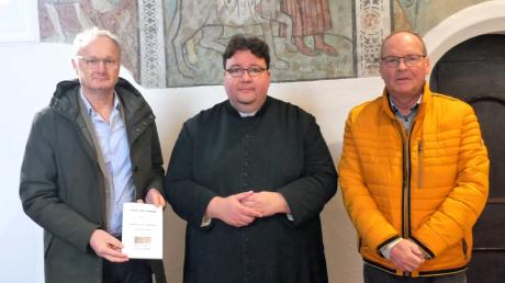 Autor Rainer Wilhelm (links) und Kirchenpfleger Helmut Kugelmann (rechts) präsentieren Pfarrer Jörg Biercher die Staudheimer Bilderbibel, dahinter ein Teil der Freskos „Flucht nach Ägypten“.