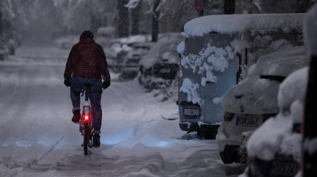 Ein Mann fährt in München mit seinem Fahrrad über eine schneebedeckte Straße.