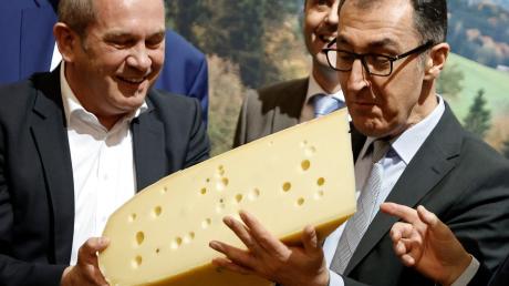 Cem Özdemir (Bündnis 90/Die Grünen) hält beim Eröffnungsrundgang über das Messegelände der Grünen Woche am Stand der Schweiz ein großes Stück Käse in Händen. 