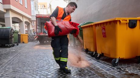 Ein Feuerwehrmann verteilt in der Altstadt von Augsburg Granulat, um Öl zu binden.