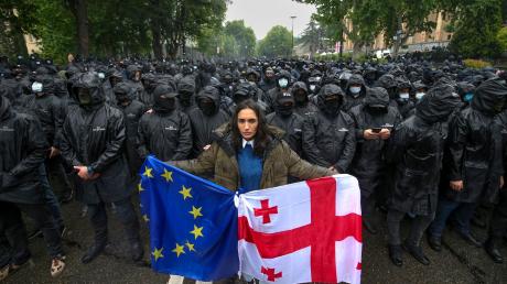 Die Proteste gegen das "russische Gesetz" und die Regierung in Tiflis gehen trotz großer Präsenz der Sicherheitskräfte weiter: Eine Frau mit einer georgischen National- und einer EU-Fahne steht vor Polizisten, die eine Straße blockieren. 