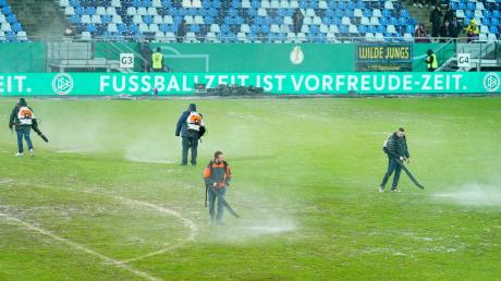 Arbeiter versuchten, Wasserlachen vom Spielfeld im Saarbrücker Ludwigsparkstadion zu entfernen.