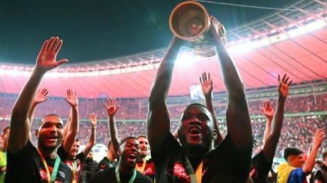 Noch ein Titel fürs ehemalige Vizekusen: Leverkusens Victor Boniface (r) hält den Pokal jubelnd hoch, während seine Teamkollegen feiern.