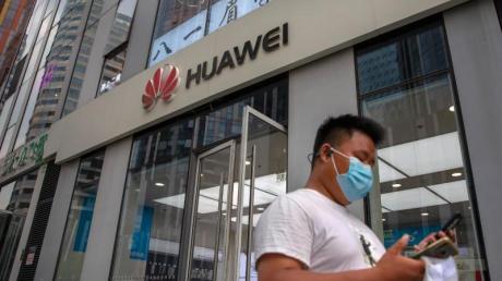 Ein Mann mit Gesichtsmaske schaut auf sein Smartphone, als er an einem Huawei-Laden in Peking vorbeigeht.