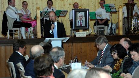Martin Sailer sprach beim Fischessen der CSU in Finningen. Im Bildhintergrund die „Schwenninger Tanzlmusi“ und ein Foto des verstorbenen früheren Landrats und CSU-Kreisvorsitzenden Dr. Anton Dietrich. 
