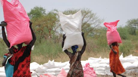 Frauen im Südsudan tragen Hirsesäcke nach Hause, die sie vom WFP erhalten haben. Die BSH Hausgeräte kooperiert jetzt mit dem Programm.  	