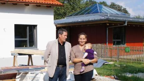 Bürgermeister Ludwig Hainzinger zeigt der Erzieherin Monika Lipp, im Bild mit ihrer Tochter Tamara, die neue Krippe. Diese ist mit dem bestehenden Kindergarten (rechts) verbunden.