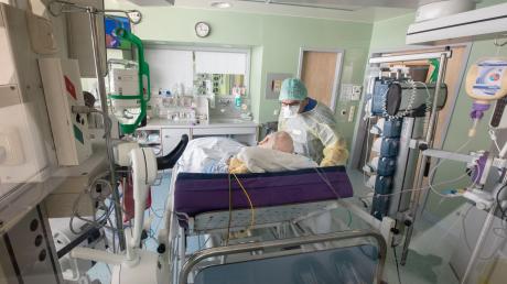 Ein Chefarzt untersucht in Schutzkleidung in einem isoliertem Intensivbett-Zimmer einen positiv getesteten Corona-Patienten.