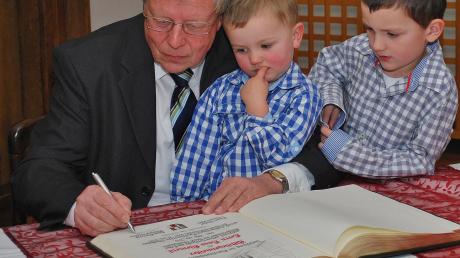 Hans Klement trägt sich in das Goldene Buch von Ichenhausen ein. Seine beiden Enkel schauen ihm dabei zu. 
