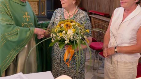 Pfarrer Johannes Rauch (links) und Brigitte Holik-Zeiser (rechts) überreichen als symbolischen Dank einen Blumenstrauß. 	 	
