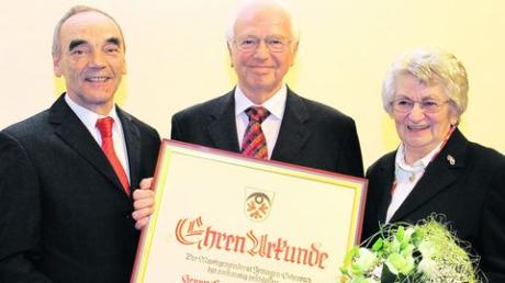 Bürgermeister Hans Reichhart (links) überreichte die Ehrenbürgerurkunde an Erwin Auerhammer und betonte, dass in die Ehrung auch dessen Frau Edeltraud (rechts) eingebunden sei. Foto: Adlassnig