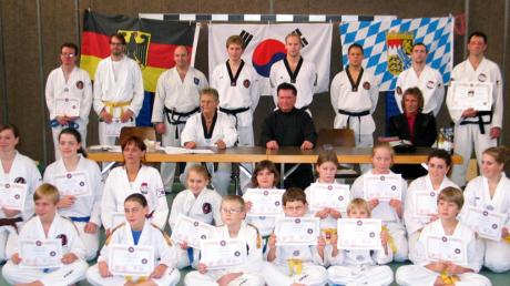 Über die bestandenen Taekwondo-Prüfungen freuten sich die meist jungen Teilnehmer. Unser Foto zeigt sie zusammen mit Erich Maier (am Tisch links) und Großmeister Jakob Beck (rechts daneben) und den Helfern.  