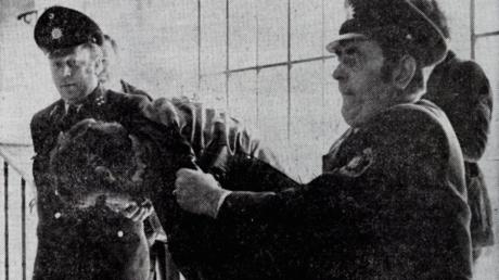 Verbirgt sein Gesicht vor dem Fotografen: Rudi R. auf dem Weg zum Haftrichter am 07.03.1975. Er ist wegen Ermordung eines Polizeibeamten angeklagt.