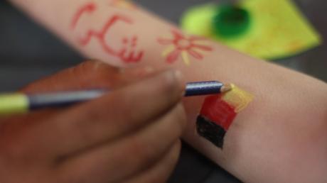 Ein Syrer schreibt in syrischer Sprache "Danke" und malt eine deutsche Fahne auf einen Arm.