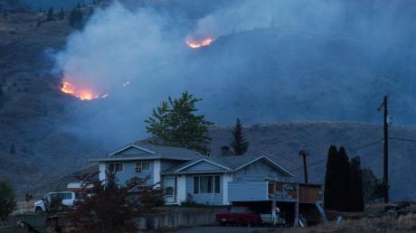 Flammen lodern am im kanadischen Ashcroft in den Hügeln hinter einem Gebäude.
