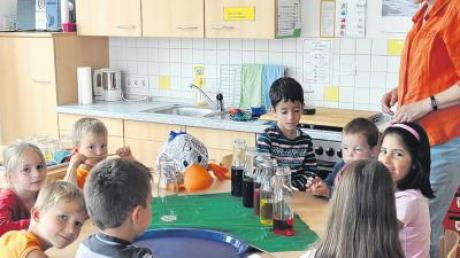 Erzieherin Ursula Wrona-Michl baut mit den Kindern der Schulvorbereitenden Einrichtung Balzhausen und Paula eine Glasorgel mit verschieden hoch gefüllten Flaschen mit buntem Wasser. 