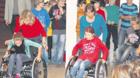Barbara Grabmair (links) und Anja Charafeldin zeigen den Fuchstaler Schulkindern, wie schwer es ist, im Rollstuhl über eine Schwelle zu gelangen.  