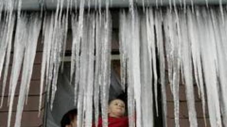 Eine Frau mit Kind schaut in Fichtelberg (Landkreis Bayreuth) aus ihrem von Eiszapfen verhangenen Fenster. 