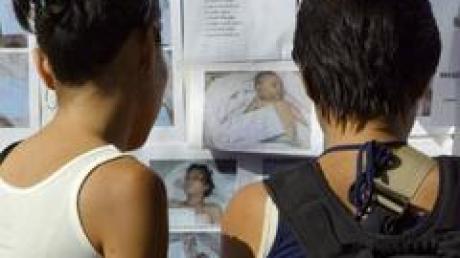 Angehörige von Vermissten vor einer Fotowand mit Bilder von Flutopfern.