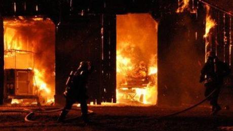 Ein Feuerwehrmann bekämpft die Flammen, die aus einem Stadel schlagen.