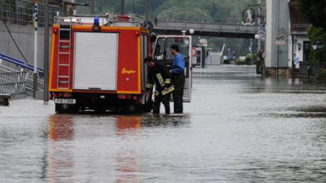 Zwei Einsatzkräfte stehen am Donnerstag (03.06.2010) in Passau (Niederbayern) neben einem Feuerwehrwagen in einer von der Donau überfluteten Straße.