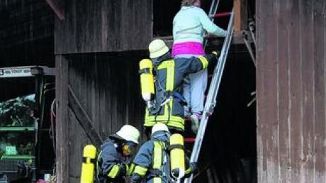 Die Feuerwehrleute retten eine verletzte Person aus dem brennenden Stadel.