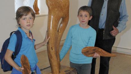 Maxi (links) und David nahmen mit anderen Kindern an den Kindermuseumstagen und der Ausstellung „Holzgeflüster“ teil. Sie stellten unter Anleitung des Holzbildhauers Siegfried Dettler (rechts) kleine Kunstwerke aus Olivenholz her.  
