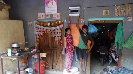 Sarvantara, ein indisches Dorf in Uttar Pradesh, wurde mit einer fotovoltaikbetriebenen DC-Mini-Grid-Anlage mit hybridem Speicher ausgestattet. Auf dem Foto: ein angeschlossener Haushalt in Indien und zwei Kinder der Familie, die auf den Powermeter zeigen. 