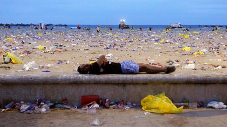 Reste einer Party: Dieser Spanier schläft in Valencia am Strand. Hinten am Meer ist schon die Müllabfuhr unterwegs.