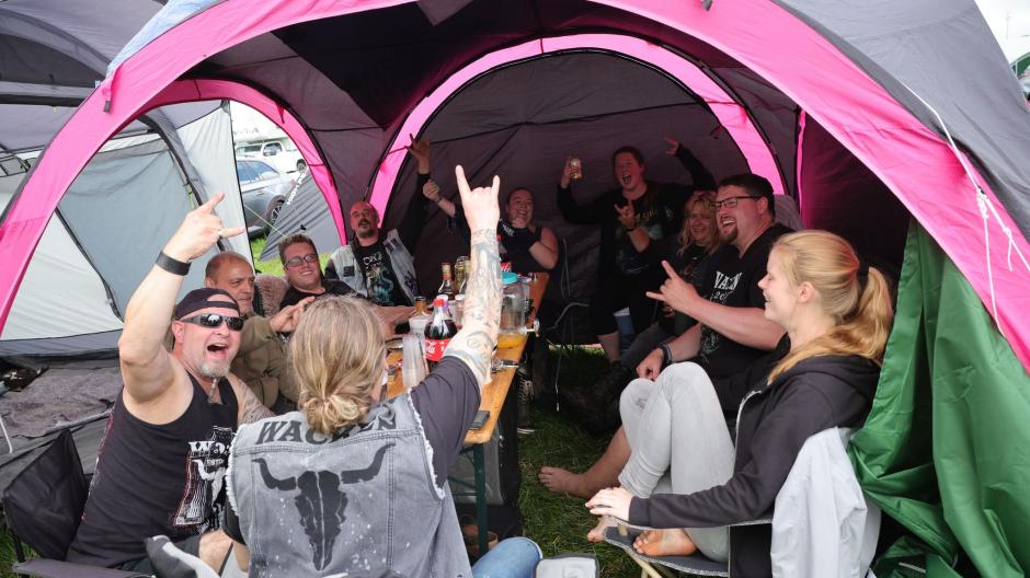 Metal-Fans aus Kiel feiern auf einem Zeltplatz auf dem vom Regen aufgeweichten und schlammigen Festivalgelände