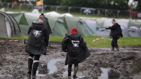Metal-Fans sind auf dem schlammigen Festivalgelände unterwegs.