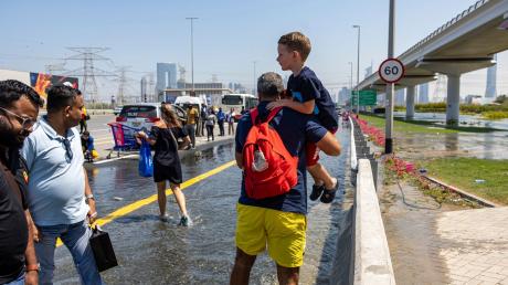 Ein Mann trägt ein Kind durch das von starkem Regen verursachte Hochwasser in Dubai.