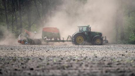 Ein Landwirt fährt mit einer Sämaschine am Traktor über ein trockenes Feld und zieht eine Staubwolke hinter sich her.  