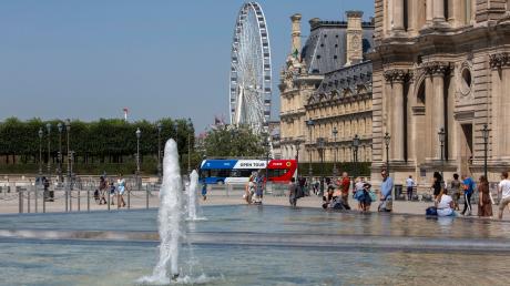 Passanten kühlen sich neben dem Brunnen vor dem Louvre in Paris ab.
