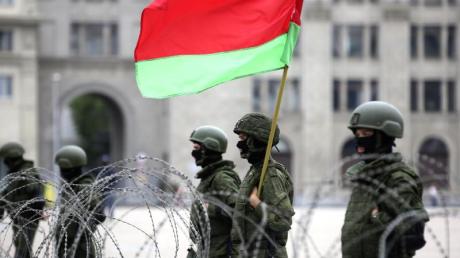 Uniformierte Sicherheitskräfte stehen in Minsk mit der belarussischen Staatsflagge hinter Stacheldraht.