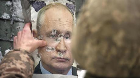 Ein ukrainischer Soldat justiert ein von Kugeln durchlöchertes Bild des russischen Präsidenten Putin.
