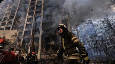 Einsatzkräfte der Feuerwehr stehen in Kiew vor einem brennenden Wohngebäude, dass durch Bombenbeschuss des russischen Militärs zerstört wurde.