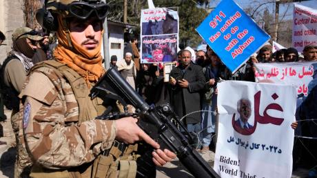 Ein bewaffneter Taliban-Kämpfer steht während einer Demonstration neben afghanischen Demonstranten.