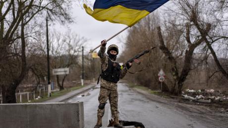 Ein ukrainischer Soldat steht an einer Straßenblockade und hält die ukrainische Flagge hoch.