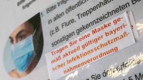 Ein Aufkleber mit der Aufschrift „Tragen Sie eine Maske gemäß aktuell gültiger bayerischer Infektionsschutzmaßnahmenverordnung“ ist an einem Hinweisschild im Amtsgericht in München zu sehen.