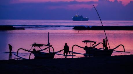 Männer befestigen vor Sonnenaufgang am Tag vor Beginn des G20-Gipfels am Strand von Nusa Dua Boote. Im Hintergrund ist ein Schiff der indonesischen Marine zu sehen.