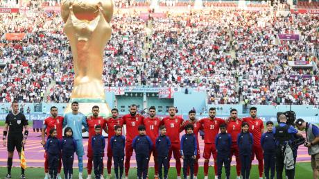 Spieler des Iran stehen beim Abspielen der Nationalhymne vor dem übergroßen Weltpokal im Stadion in Katar. Sie blieben stumm, ein Zeichen.