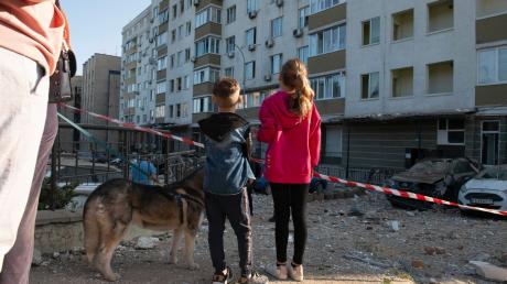 Kriegsalltag: Kinder schauen in Kiew auf ein bei russischen Raketenangriffen beschädigtes Gebäude.