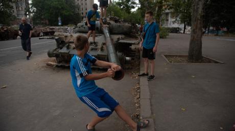Jungen spielen an einem zerstörten russischen Panzer, der auf einer Straße von Mykolajiw steht.
